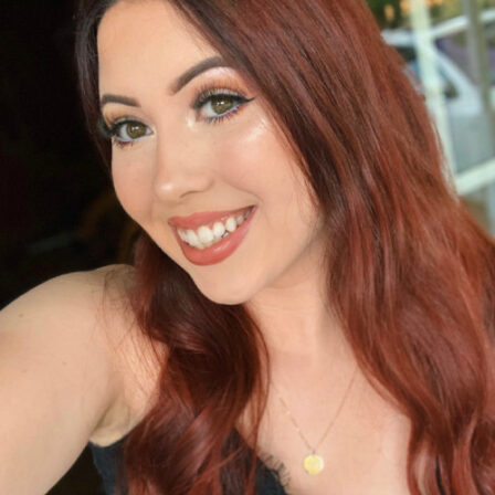 Samantha Kinney, a smiling young woman with long straight auburn hair, wearing a gold necklace and a black shirt