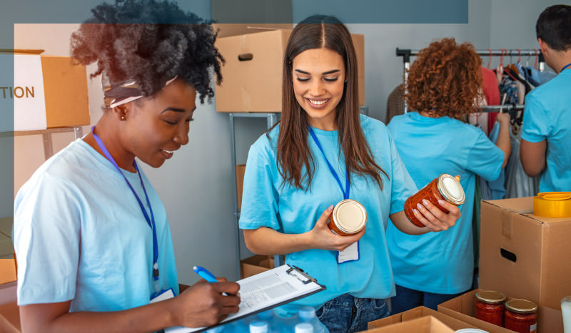 Volunteers wearing blue t-shirts, packing canned food in boxes and marking it on clipboard