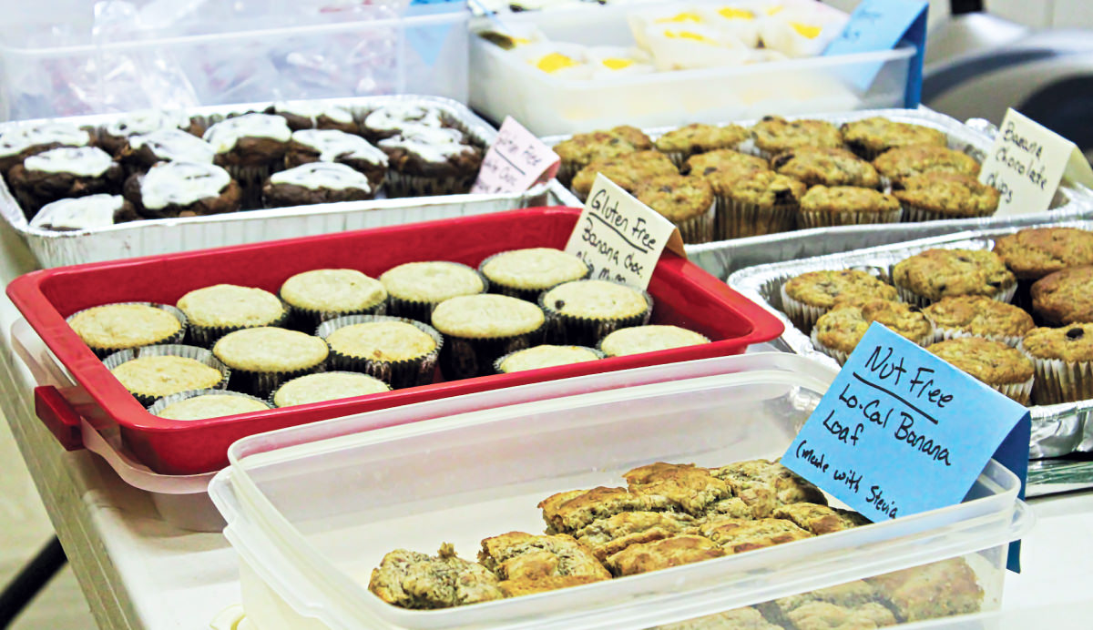 Baked goods in silver, red, and clear containers on a table, with signs attached to them