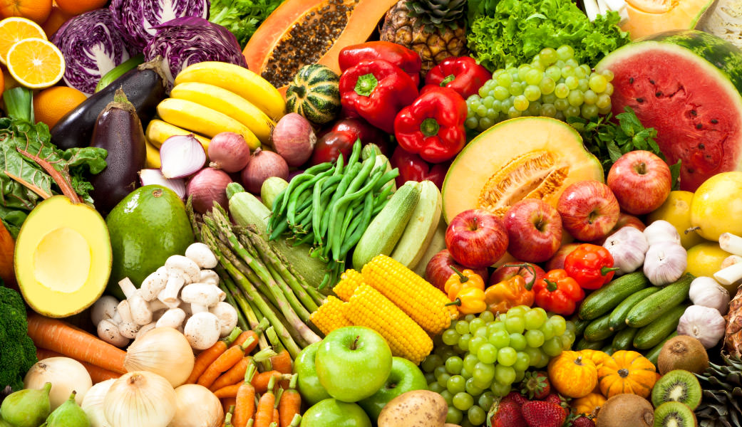 Assorted fruits and vegetables piled together including apples, corn on the cob, mushrooms, bananas, watermelon, peppers, garlic, kiwi, strawberries and more