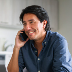 Man with black hair, wearing a blue shirt, smiling, and talking on the phone