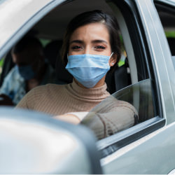 young woman in car with the window down wearing a blue disposable mask