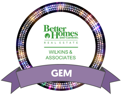 Better Homes and Gardens Real Estate Wilkins & Associates logo surrounded by a black outer circle filled with gem sparkles, and a purple Gem Sponsor ribbon at the bottom