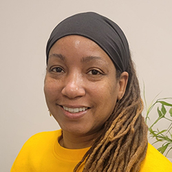 Tyiesha Hinton, Ph.D., a smiling woman with long hair standing in the office beside a plant