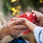 Young person handing a wrapped gift to an elderly woman.