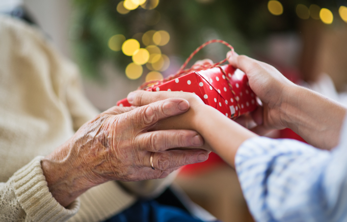 Young person handing a wrapped gift to an elderly woman.